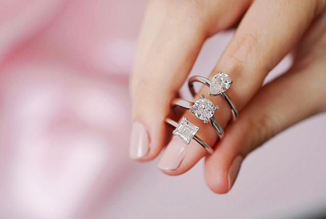 Hand met drie witgouden verlovingsringen met diamant: peer-, ronde en prinses slijpvorm 3 ringen van BAUNAT