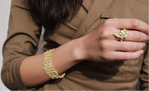 Een vrouw met een gouden schakelarmband en een gouden ring aan haar hand, met de nadruk op elegante fijne sieraden.