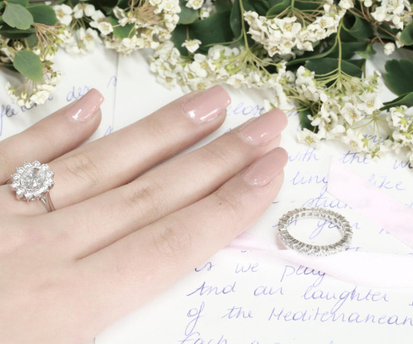 Hand met witgouden ring met ovale diamant omringd door halo van kleinere diamanten