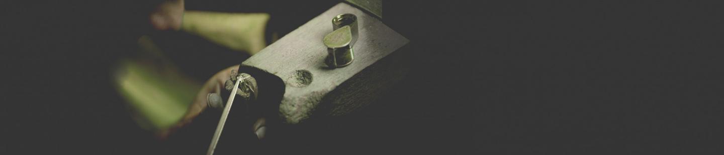 珠宝工坊中，工匠用金属工具固定一枚戒指托座，银白色金属表面细节清晰，呈现戒指制作过程的特写。
