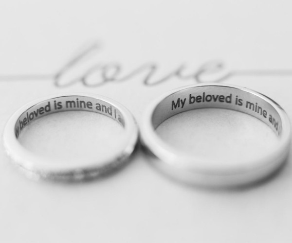 两枚银色抛光结婚对戒，内圈刻有英文“My beloved is mine and I…”，简约圆弧宽版设计，黑白背景静物展示