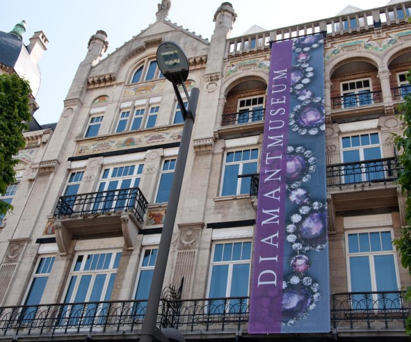 安特卫普钻石博物馆外立面，古典建筑上悬挂紫色“DIAMANTMUSEUM”竖幅海报，展示钻石珠宝主题