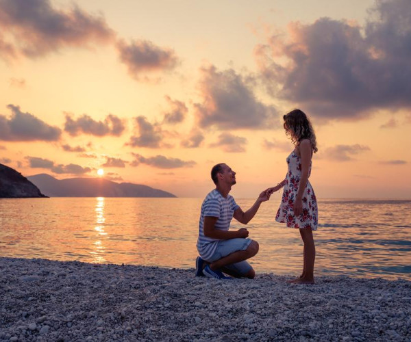 海边日落时分，男子单膝跪地向女子求婚，手持戒指，浪漫海景与金色晚霞背景